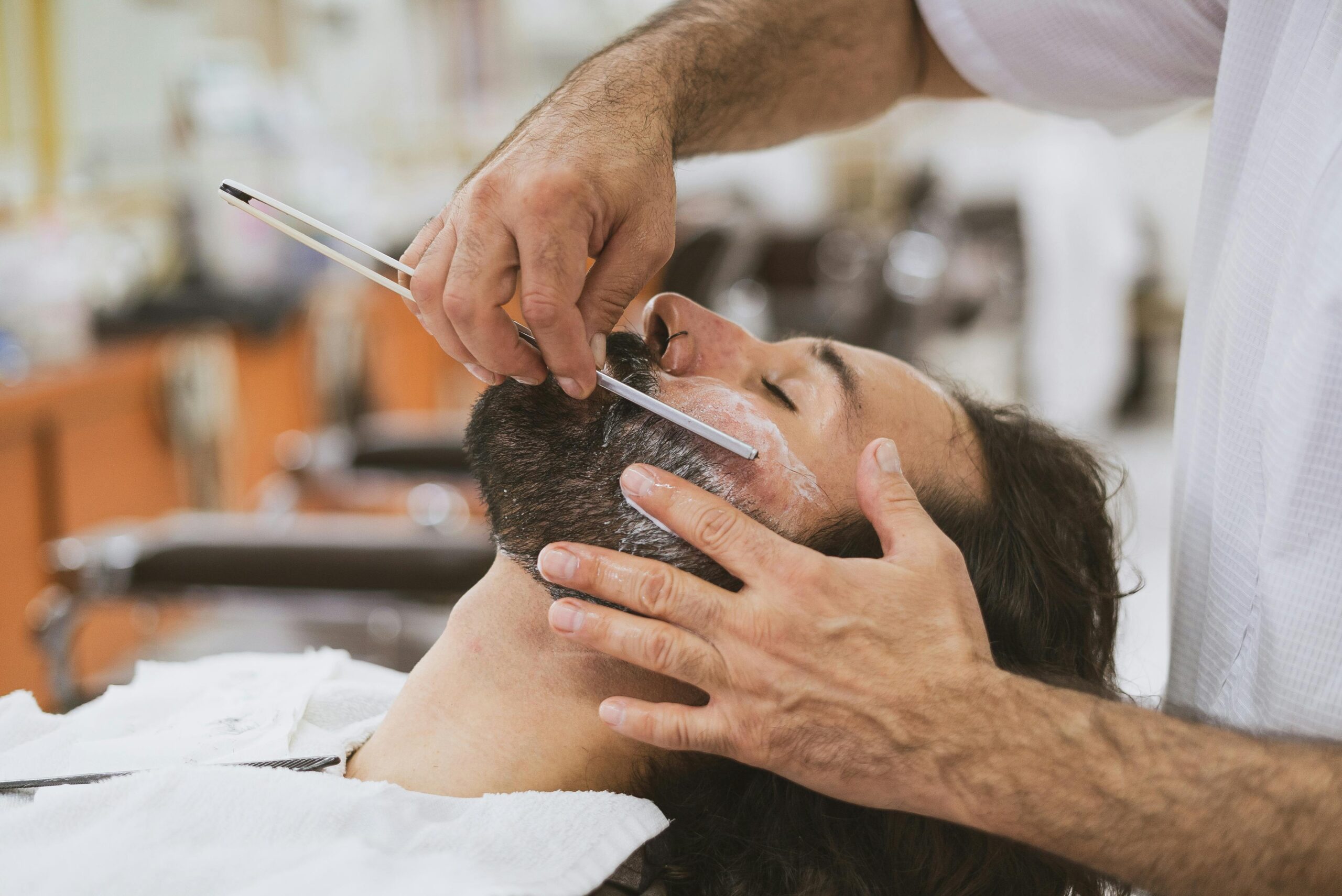 Barber performing a classic shave with a straight razor. Facial grooming in a barber shop.