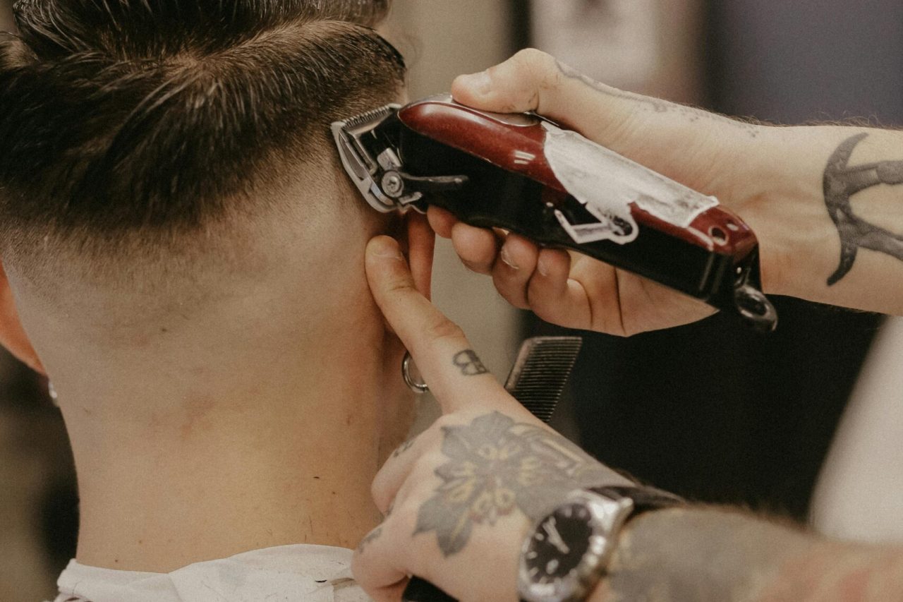 pexels-photo-4351728-4351728 A tattooed barber uses electric clippers for a stylish haircut on a customer in a barber shop.